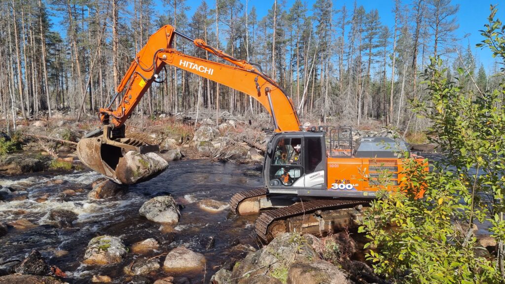 Excavator moving a big boulder in a river.