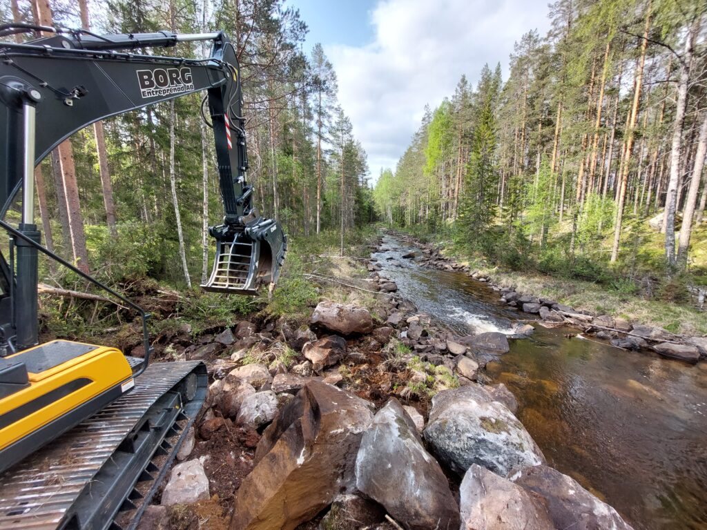 Ett vattendrag som är mycket rensat på sten och block. En grävmaskin syns närmast i bild.