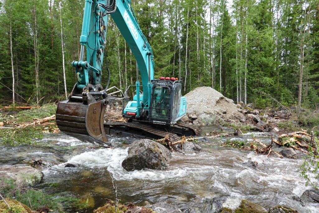 Excavator in the watercourse with large boulders.