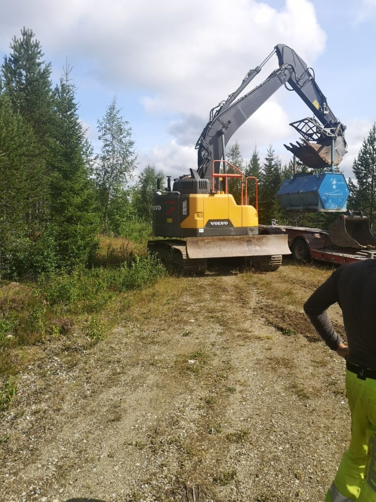 En grävmaskin som lyfter en liten container med skopan